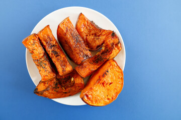 A plate of roasted butternut squash served on a blue background, garnished with herbs and spices. 
