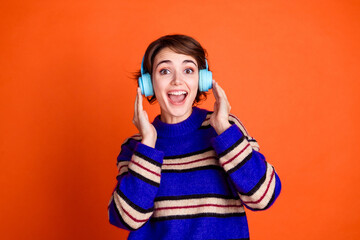 Photo of millennial woman brown haired model wearing striped jumper enjoying her new wireless headphones isolated on orange color background