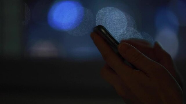 夜の暗い部屋でスマートフォンを見ている女性　窓から見える夜景　室内