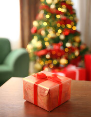 A close-up of a Christmas gift resting on a table, with a beautifully decorated Christmas tree softly blurred in the background of the living room