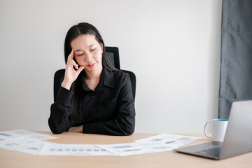 A businesswoman in a black shirt sits at a desk reviewing financial documents, deep in thought, in a contemporary office environment.