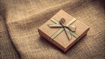Elegant gift box with bow on burlap fabric background.