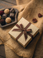 Elegant gift box with brown ribbon and assorted truffles on burlap fabric.