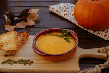 Close up view of a pumpkin soup in a bowl served with pumpkin seeds and croutons. Vegan soup. Rustic wooden background