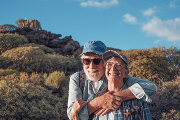 Cheerful caucasian senior couple with backpack and cap enjoying trekking day in countryside admiring landscape, Healthy lifestyle in retirement concept