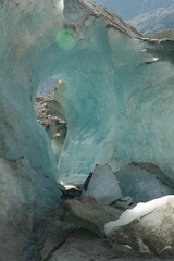 A stunning glacier cave showcasing vivid blue ice formations and rocky textures, illuminated by sunlight streaming through natural openings, creating a surreal, frosty landscape.