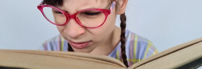 Girl with glasses with poor eyesight reads book. Farsightedness and myopia in children and...