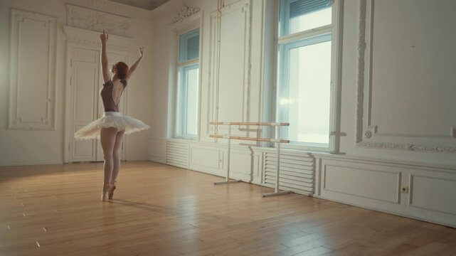 Slender graceful ballerina in tutu dancing in rehearsal room, slow motion. Attractive female ballet dancer exercising in dance hall, standing on parquet with pointe shoes, classical dance performance
