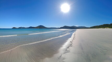 Tranquil beach scene with clear water and bright sun in blue sky