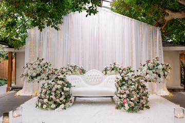 Beautiful decor for a wedding ceremony in oriental style. White sofa decorated with roses and floating candles for a wedding ceremony. Beautiful place for the bride and groom