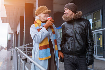 Happy senior couple walking and drinking coffee outdoors in winter