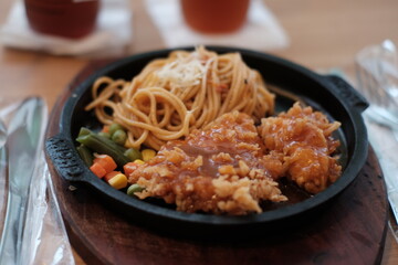 A delicious combination of crispy chicken and flavorful noodles served on a sizzling plate with vegetables