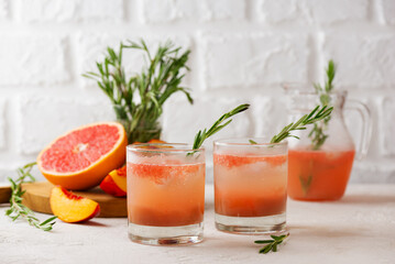 Grapefruit and peach lemonade with rosemary and ice on a light table. Healthy drink, sugar and alcohol free.