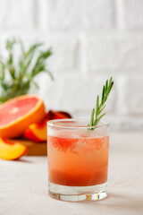 Grapefruit and peach lemonade with rosemary and ice in a glass. Healthy drink, sugar and alcohol free. Vertical orientation.