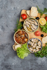 Assortment of open different canned fish with vegetables and herbs on a dark background. Sardines, sprats, sprat in tomato and oil