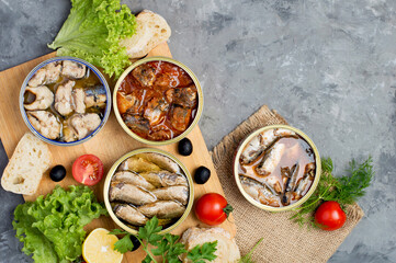 Assortment of open different canned fish with vegetables and herbs on a dark background....