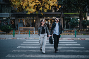 Two business people walk confidently across the zebra crossing, dressed in fashionable autumn...