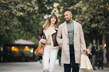 A joyful couple spending quality time shopping together, walking arm in arm down a tree-lined city...