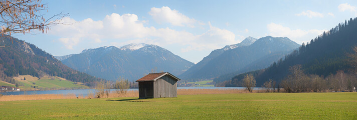 wide meadow with hut at lake shore Schliersee, view to Mangfallgebirge alps with Brecherspitze...