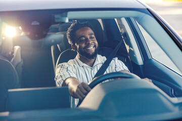 Smiling young black man driving his luxury car in traffic on a city street.