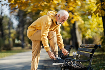 An old sportsman tying shoelace and preparing for outdoor practice in park.