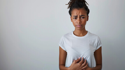 Mujer joven con expresión de incomodidad, sosteniéndose el abdomen con ambas manos, fondo claro minimalista.