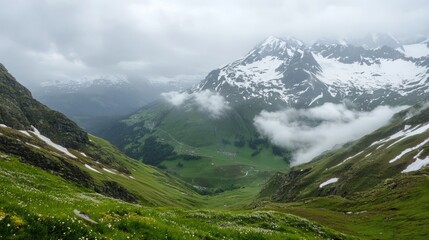 Fototapeta premium Mountain valley landscape with meadows, snow, and clouds.