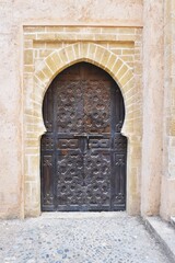 Heavy wooden door with intricate carved Moroccan design set in weathered stone archway
