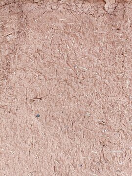 Close-up detail of adobe mud wall construction background pattern with small pebbles and short pieces of straw embedded in the surface