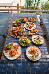 Variety of food on blue tiled surface, include with salad, salmon steak, pork chop, chicken baked, fried fish, fried rice