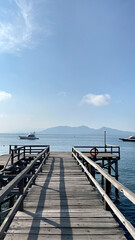Obraz premium Rustic dockyard wooden deck footpath on the open water, with beautiful mountain background, vast blue sea, under a clear sunny blue sky. Beautiful landscape and holiday feel.