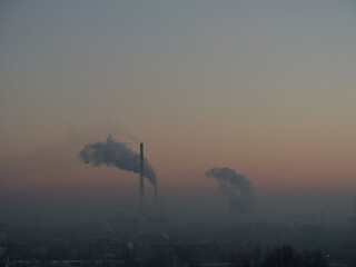 Industrial skyline at dusk with smoke rising from chimneys. Air pollution and hazy atmosphere highlight environmental impact and urban emissions © Maciej Bonk