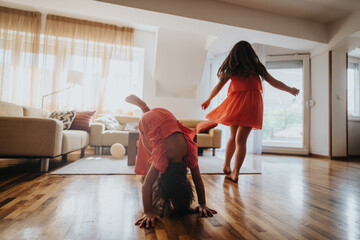 Two young girls in red dresses enjoy playful activities in a bright and cozy living room with...