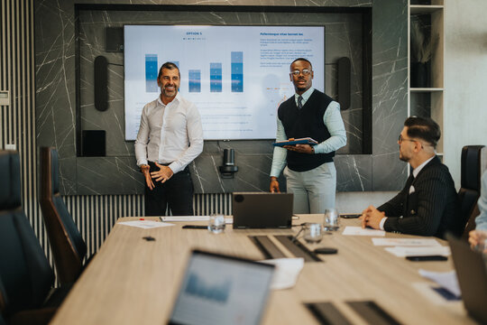 A diverse group of business people engage in a collaborative discussion, analyzing data and strategies, in a contemporary office setting with advanced presentation technology for effective
