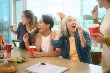 Group of cheerful coworkers gathered around table, enjoying snacks and drinks during casual office party