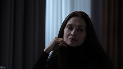 Woman suffering mental health issues, sitting at the table at camera, depressed expression, looks with contempt and irony, close view.