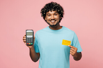 Young Indian man he wear blue t-shirt casual clothes hold wireless modern bank payment terminal to...