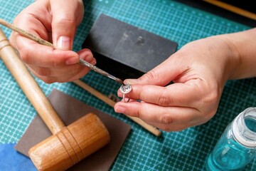 Woman crafting handmade silver ring in workshop. Ring making process in jewelry workplace.