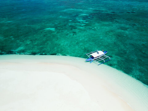 An aerial view of a traditional Filipino outrigger boat (bangka) anchored on a pristine white sand beach, surrounded by clear turquoise waters in Balabac, Philippines