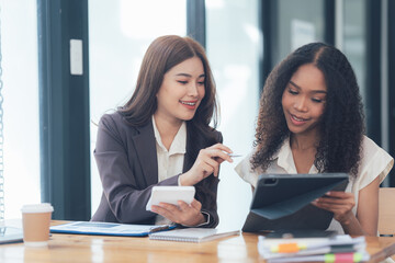 Collaborative Innovation: Two professional women engage in a productive discussion, analyzing data on a tablet and notepad, fostering a collaborative and innovative work environment.  