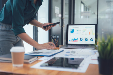 Analyzing Data: A business professional examines financial data on a laptop and tablet, surrounded by other work essentials in a modern office setting.