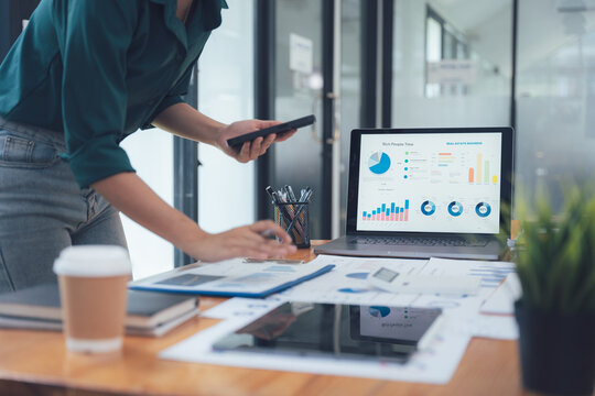 Analyzing Data: A business professional examines financial data on a laptop and tablet, surrounded by other work essentials in a modern office setting. - Powered by Adobe
