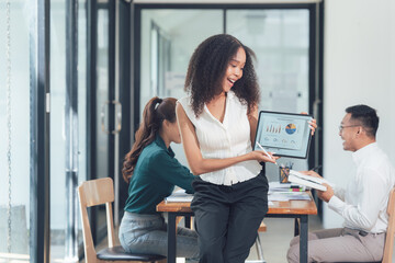 Successful Business Presentation: A young, enthusiastic businesswoman shares exciting data on a tablet during a lively team meeting.  Her colleagues react positively to the successful presentation.