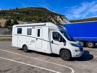 Modern camper van parked in a rest area near a truck with mountain landscape on background,...