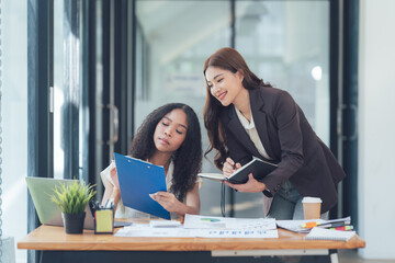 Collaborative Success: Two Businesswomen reviewing documents together at modern office desk.  