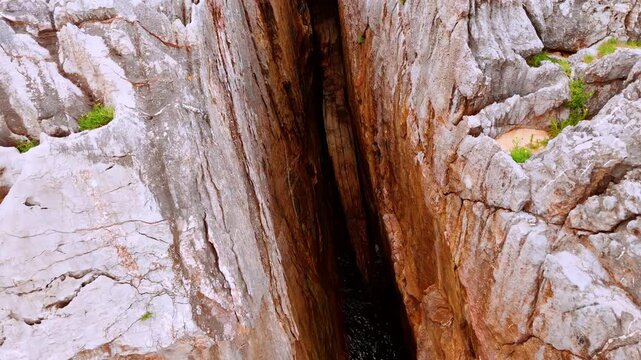 A huge gap among the high rocks filled with water. Dangerous steep cliffs from aerial perspective.