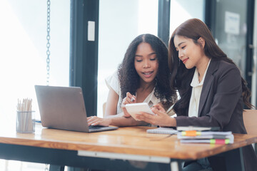 Collaborative Success: Two businesswomen review data on a calculator and laptop, showcasing teamwork, focus, and shared success.  