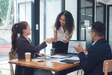 Business Handshake: A diverse team of professionals celebrates success with a handshake and applause in a modern office setting.  The image captures the joy and camaraderie of teamwork.
