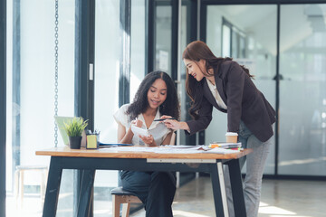 Collaborative Success: Two diverse businesswomen are engaged in a constructive conversation, reviewing documents and ideas together in a modern office setting.