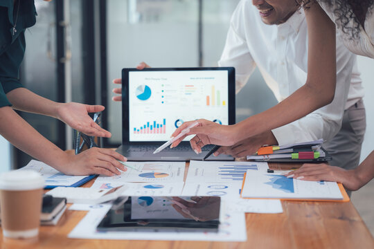 Collaborative Data Analysis: A diverse team of business professionals collaborates over a laptop and printed charts, analyzing data and discussing strategy in a modern office environment.  